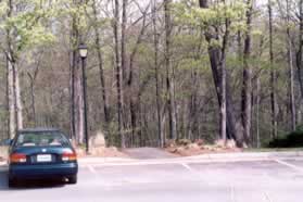 At the point where the sidewalk turns to the right turn left to cross the street to the asphalt path that enters the woods.