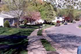 An asphalt trail intersects from between homes on the left.  Continue on the sidewalk along the street.