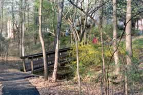The trail crosses a bridge and goes up a hill between houses.