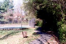 Continue straight on this path past the trails on both sides of the fenced court and up the hill between the houses on the other side.