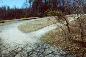 The trail enters an open area near the dam.  The asphalt trail to the left leaves the park.  Stay on the wide trail to the dam.