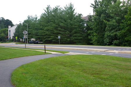 The asphalt trail turns right to cross Hunter Village Dr. in a crosswalk. Turn left to follow the concrete sidewalk along Hunter Village Dr.