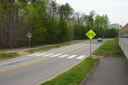 The asphalt trail ends. Turn left to cross Hunter Village Dr. in the crosswalk. Turn right to follow the asphalt trail on the other side.