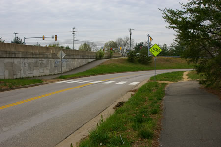 The asphalt trail ends. Turn left and use the crosswalk to reach the asphalt trail on the other side of Hunter Village Dr. and follow it to the right.