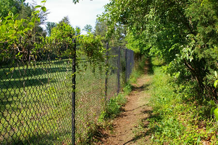 The trail follows a fence next to the golf course. There is also a fence on the right.