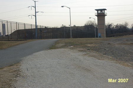 The gravel trail joins an access road around the prison. Turn right to follow that road with the prison fence on your left.