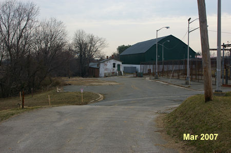 An access road intercepts from the left . Turn left to follow this road away from the prison fence.