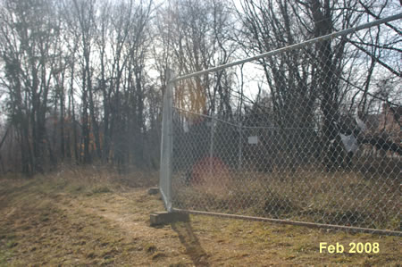 The first watchtower is separated by a fence. Walk to the left around the fence and follow a short detour into the woods and back to the prison access road.
