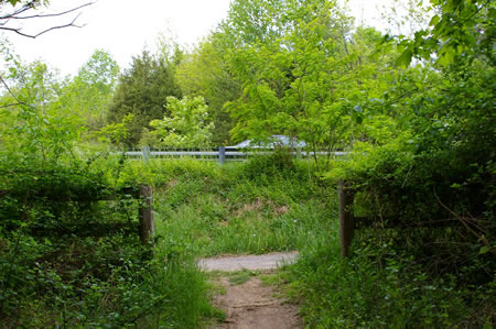 The dirt trail intersects with an asphalt trail through an opening in a fence just prior to Vale Rd.