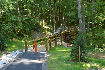 The trail utilizes a curved ramp to reach the bottom of the hill where it crosses a bridge.