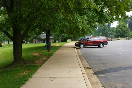 The trail connects to a concrete sidewalk along the edge of a parking lot. Follow the sidewalk to the first building on the left.