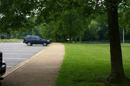 Take the short walkway from the back of the building to the parking lot and turn right to follow the walkway along the parking lot.