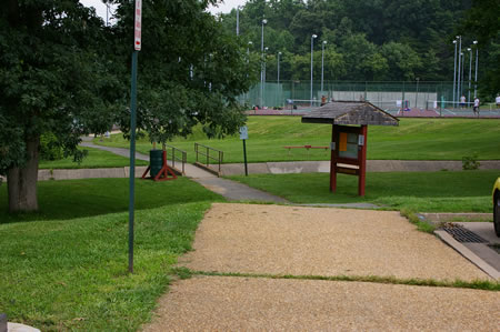 The sidewalk leads into an asphalt trail back towards the tennis courts.