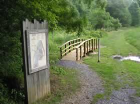 Turn left to cross the bridge and follow the trail through the open field.