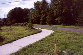 The sidewalk along the street turns left away from the street.  Remain on the sidewalk toward the asphalt path turning left to follow the asphalt path.