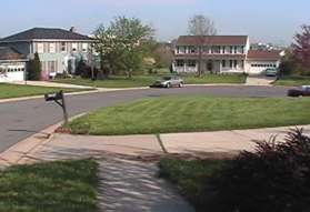 The sidewalk does not quite go to the end of the street.  There is an asphalt path at the end of the street next to the car in the picture.  Take that path.