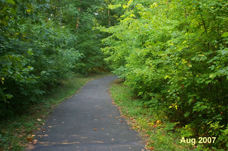 The asphalt trail passes behind homes on the left.