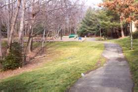 The sidewalk joins a wide asphalt path and a play area appears on the left.  Continue straight on the asphalt path.