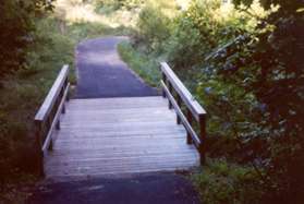 The trail crosses a stream on a bridge and turns right.